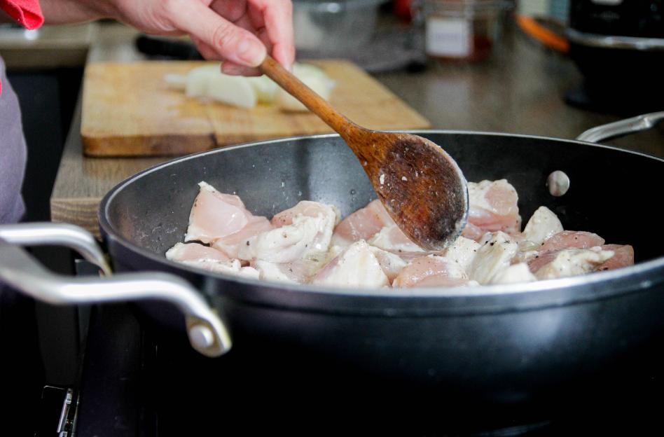 A person cooks chicken in a frying pan.