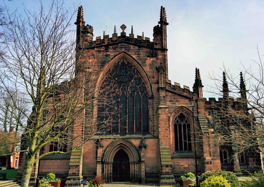 A stone church with a large arched window above the entrance, flanked by bare trees.