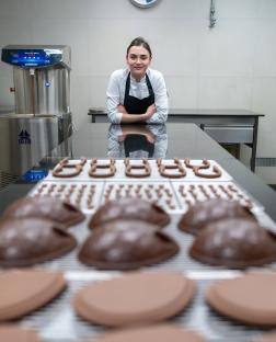 A chocolatier poses in front of trays of chocolate eggs.