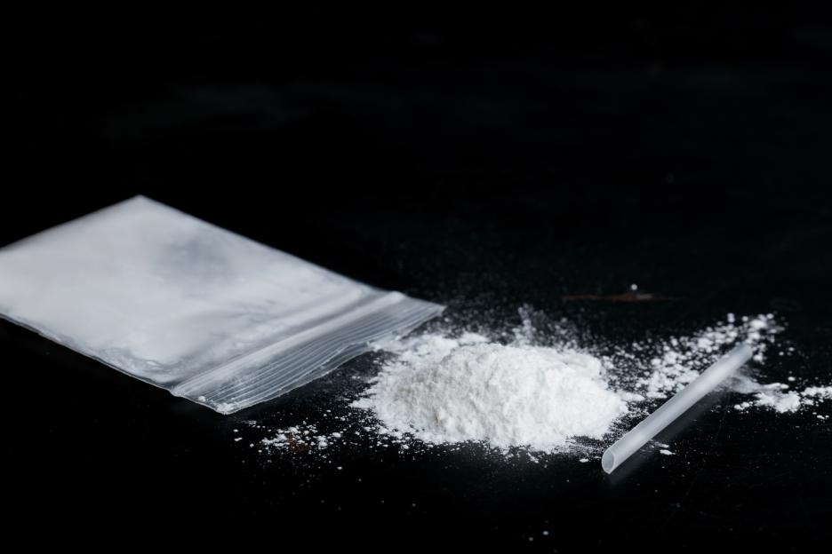 Ketamine drugs and plastic straw on bag of white powder on black wood background.
