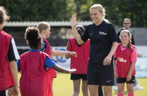 A woman high-fives young girls at a Fun Football event.