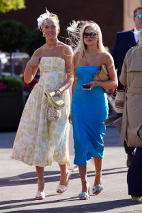 Two women in stylish dresses and floral-adorned heels at a horse race.