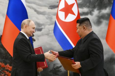 Vladimir Putin and Kim Jong Un shaking hands at a signing ceremony.