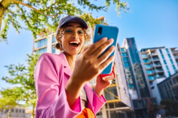A surprised woman looking at her phone outdoors.