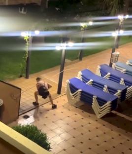 Video grab of a person sneaking around a stack of pool loungers at night.