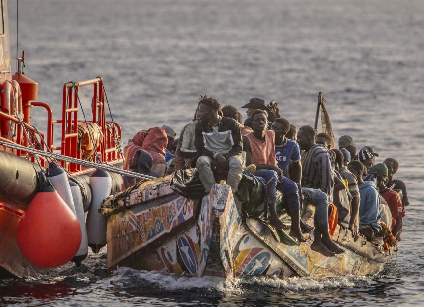 Rescued migrants on a small boat being towed by a larger vessel.