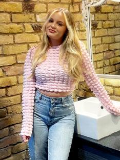 Woman in pink textured top and light wash jeans leaning on a bathroom sink.