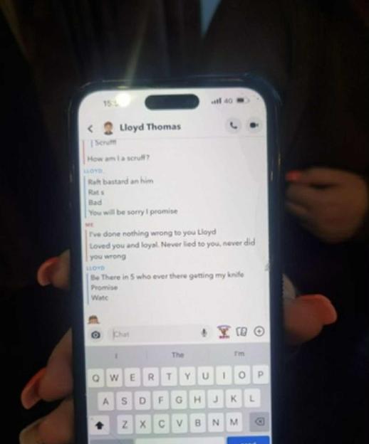 A person's hands holding a smartphone displaying a threatening text conversation with "Lloyd Thomas."