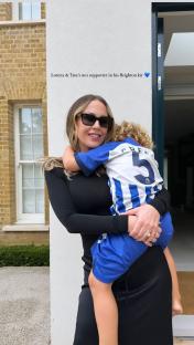 Woman holding young boy in Brighton football kit.
