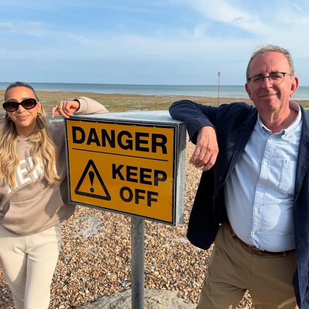 Two people posing by a "Danger Keep Off" sign on a beach.