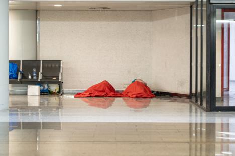 Two people sleeping under red blankets in an airport.