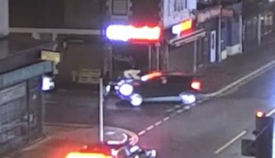 Nighttime security footage of a car at an intersection.