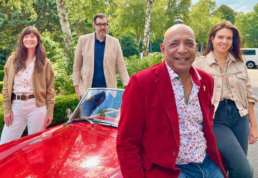 Four people standing by a red car.