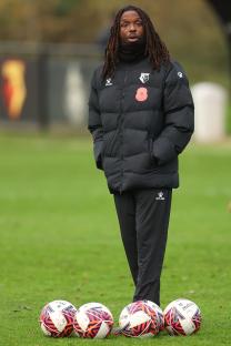 Gifton Noel-Williams, Watford coach, stands on a soccer field.