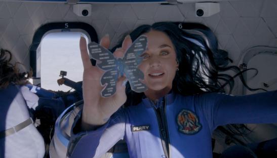 Katy Perry in zero gravity holding a butterfly-shaped cutout with song titles.