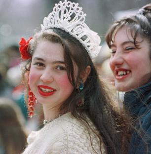 A young Romani woman smiles while wearing a tiara, awaiting selection as a bride.