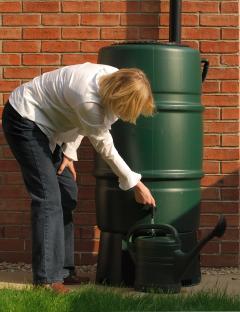 Woman filling a watering can from a rain barrel.