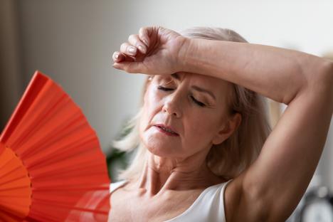 Senior woman fanning herself, looking unwell from the heat.