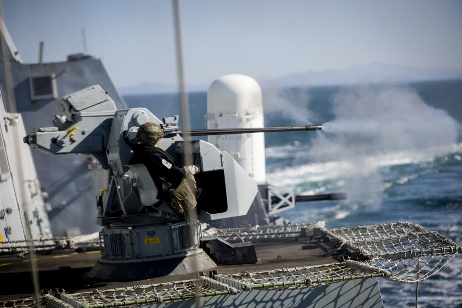 A sailor firing a gun on a ship at sea.