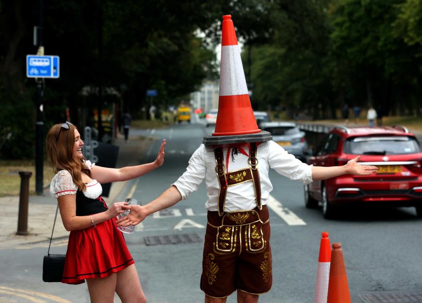 A man with a traffic cone on his head and a woman in dirndl garb during a pub crawl.
