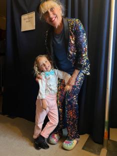 A woman in a sequined outfit and a young boy in pink pants pose together.