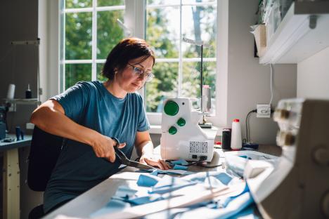 A woman cuts fabric at her sewing machine.