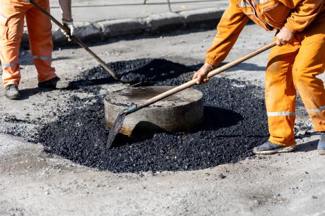 Two construction workers spreading asphalt around a manhole.