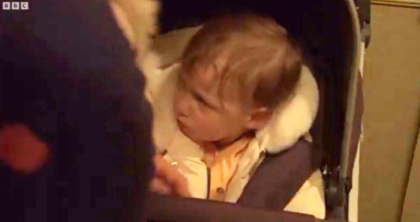 A baby in a stroller looking upset.