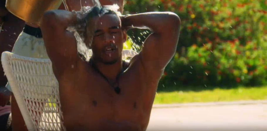 Man getting showered with water from above, holding his hands behind his head.