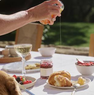 Honey being poured onto a croissant at an outdoor brunch.