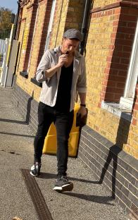 Joe Swash walking on a sidewalk while holding a vape to his mouth.