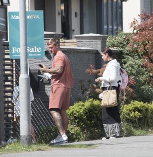 A man and woman stand outside a home; the man is looking at his phone.