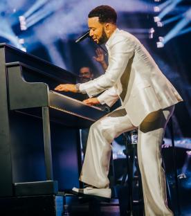 John Legend performing on stage at a piano.