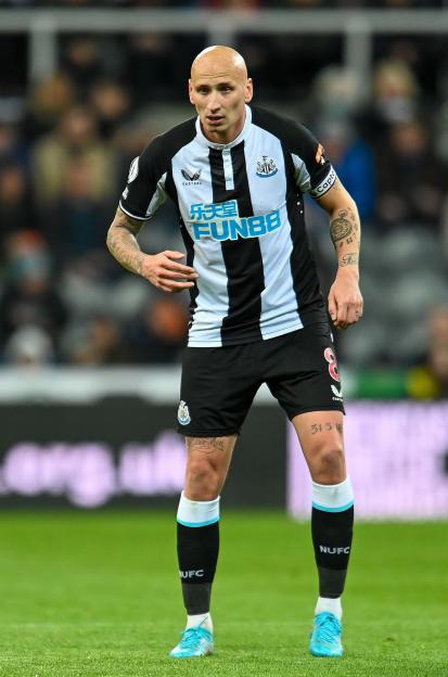 Newcastle United's Jonjo Shelvey in his team's black and white striped jersey, black shorts, black socks with a light blue stripe, and light blue cleats.