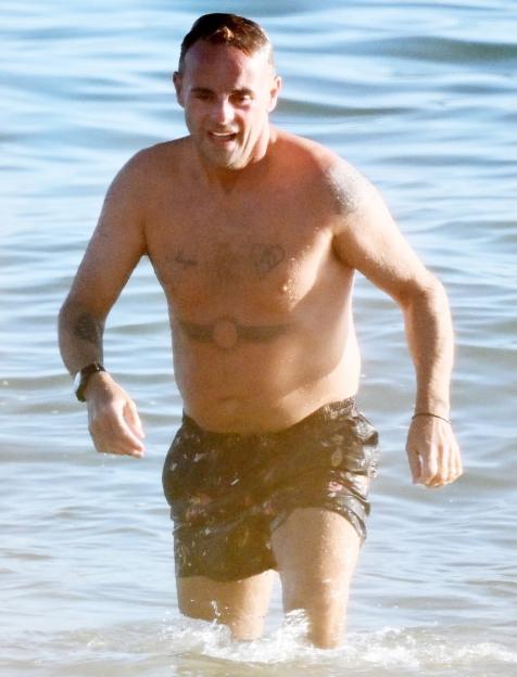 Ant McPartlin shirtless in the ocean wearing swim shorts.