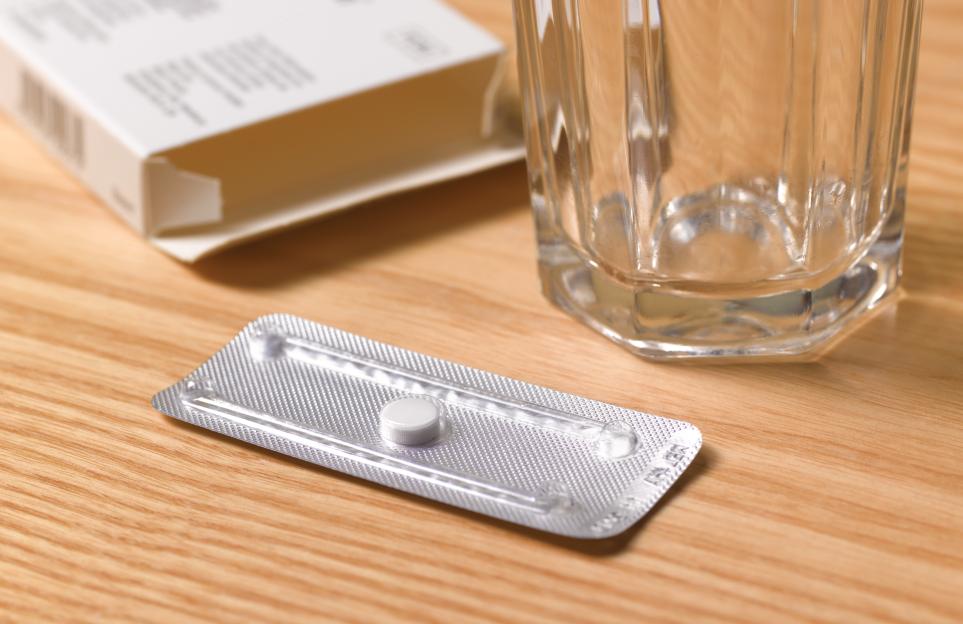 Morning-after pill in a blister pack next to an empty glass of water and the pill box.