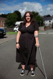 Woman in black dress using a crutch.
