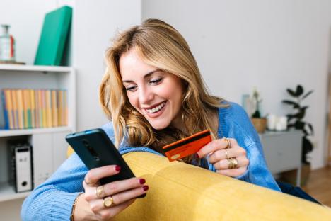 Smiling woman using a smartphone and credit card to shop online.