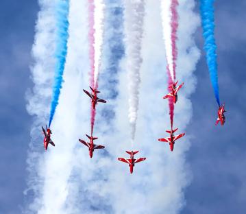 Red Arrows performing aerial maneuvers, leaving red, white, and blue smoke trails.