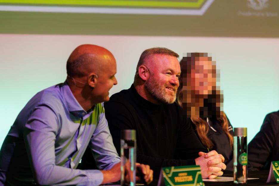 Wayne Rooney and another man smiling while sitting at a table with an obscured person.