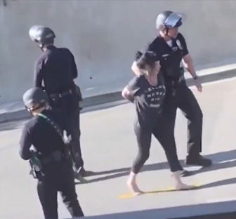 Barefoot woman in handcuffs escorted by police officers.