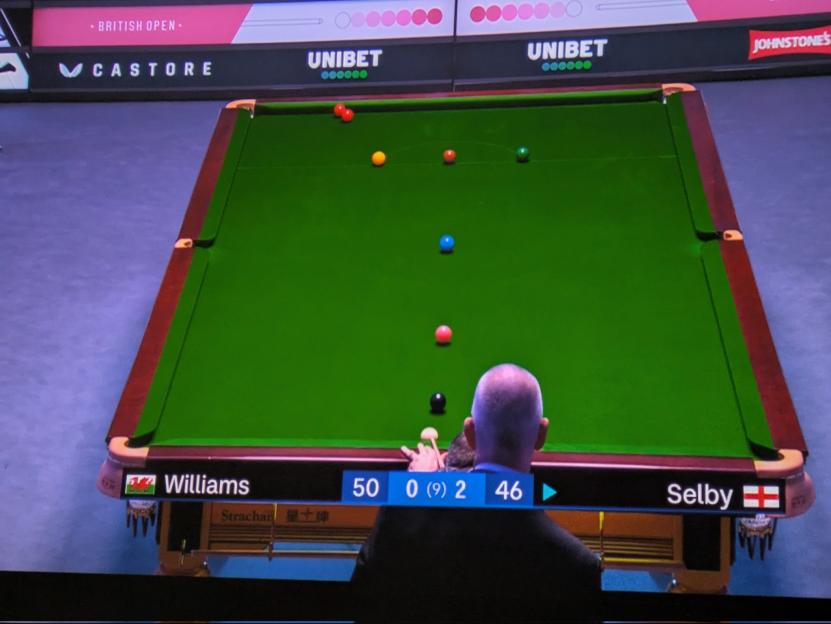 A snooker match between Williams (50 points) and Selby (46 points) in the British Open, viewed from behind Williams as he prepares to strike the cue ball.