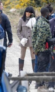 A woman in a beige jacket and brown riding boots on a film set.