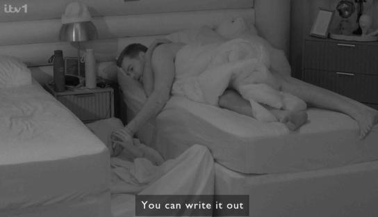 Black and white image of a person writing on a sleeping person's hand.