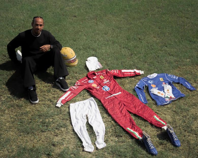 Lewis Hamilton sitting on the grass with racing gear and helmet, dedicated to Niki.