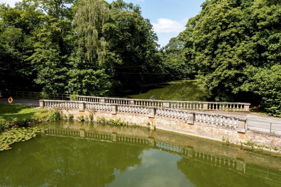 Stone bridge over a pond, surrounded by trees.