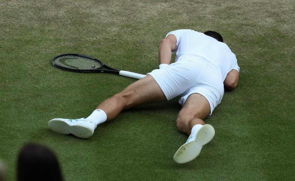 Novak Djokovic lying on a tennis court after falling during a serve.
