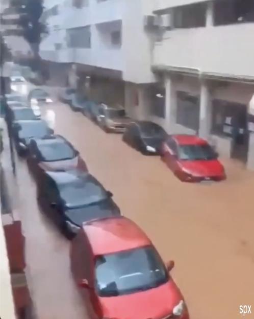 Flooding on a street in Ibiza with several cars submerged in murky brown water.