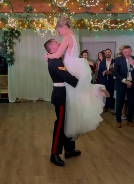 A groom in uniform lifts his bride during their first dance.