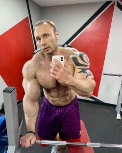 Photo of a muscular man taking a selfie in a gym.